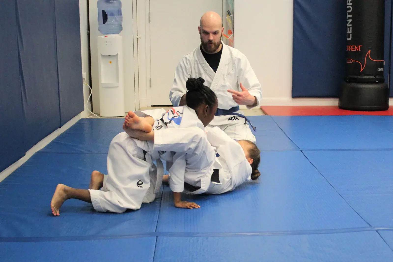 Two Jiu-Jitsu students drilling a triangle as their coach watches