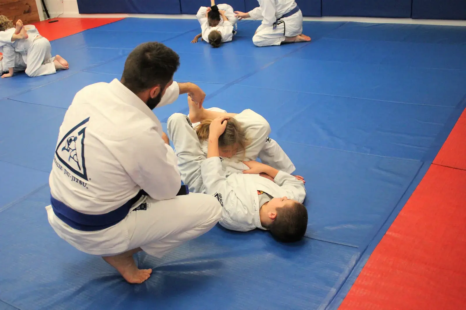 A coach teaching two Youth Jiu-Jitsu students on the mat