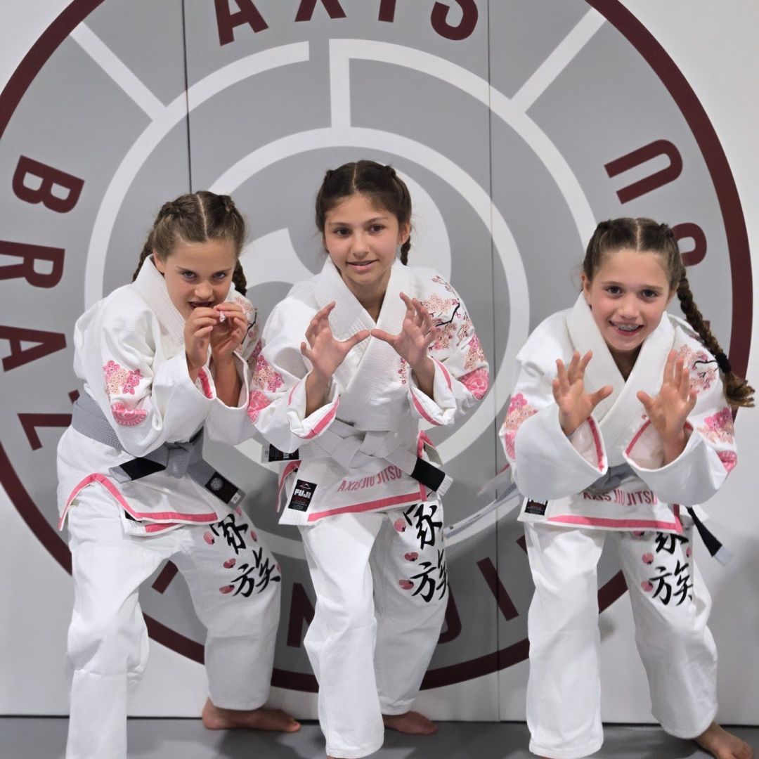 Three Axis kids in gis in front of the Axis logo