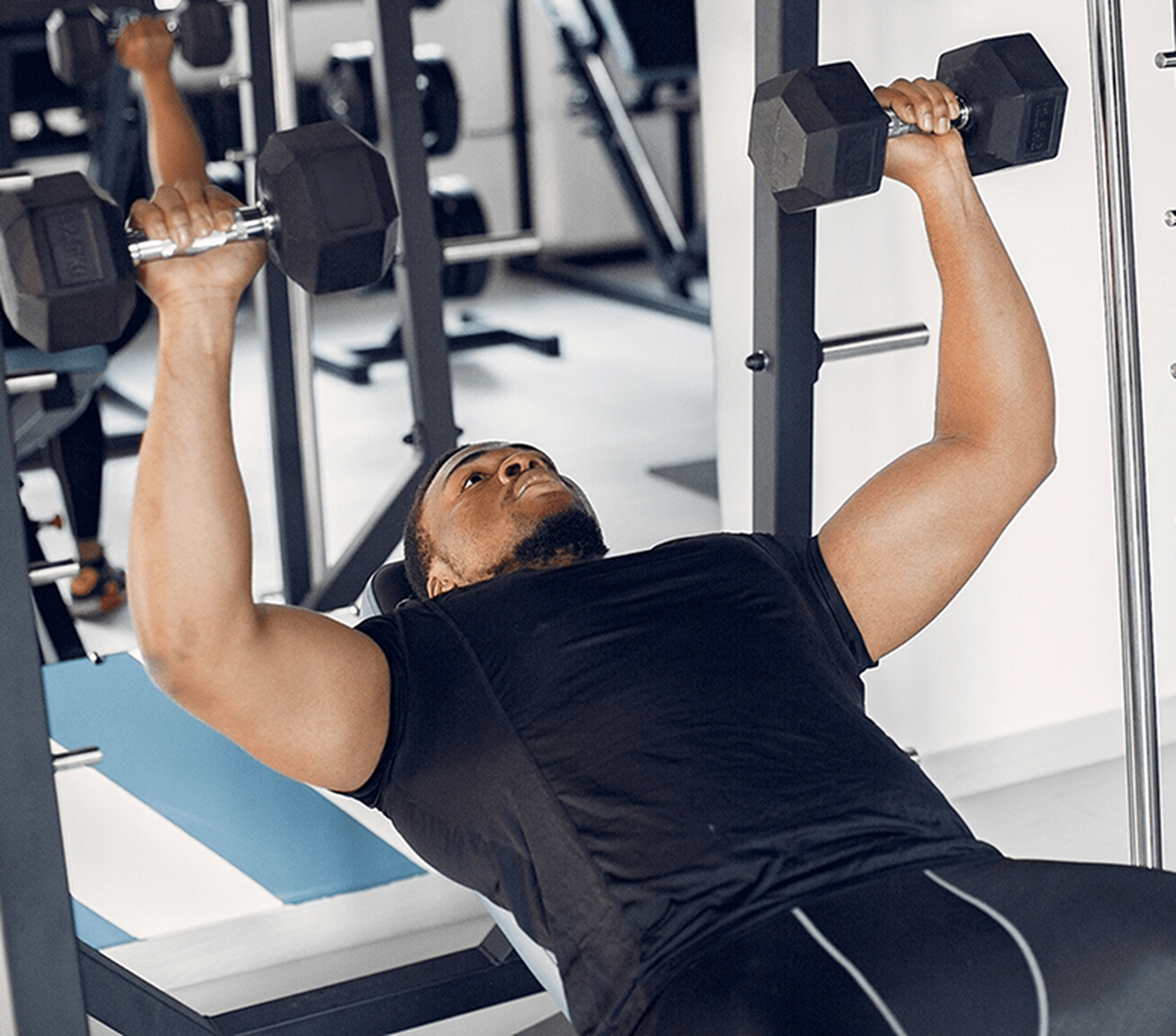 Gym member lifting dumbbells on a bench