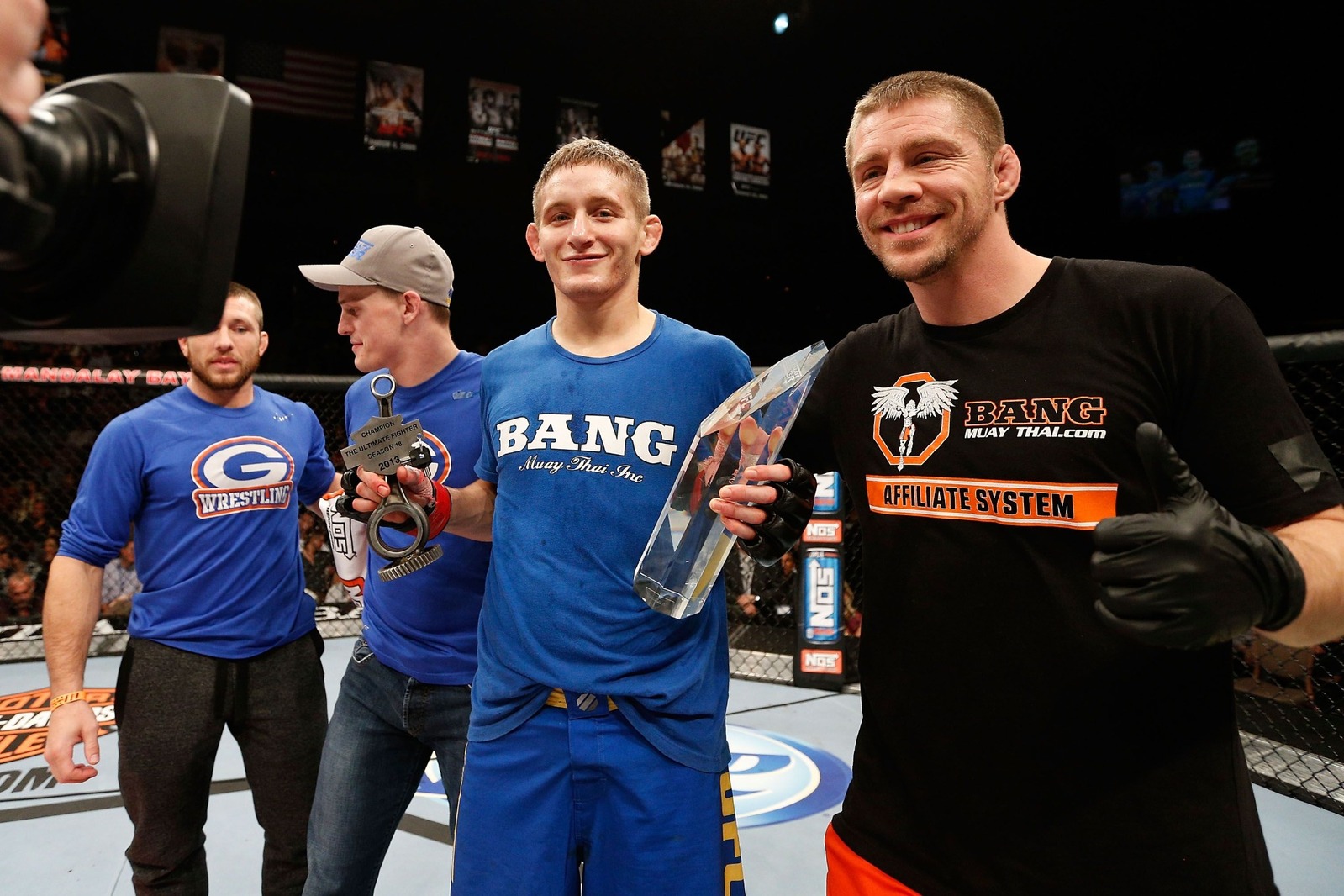 Chris Holdsworth holding his Ultimate Fighter Season 18 trophies with his team in the Octagon