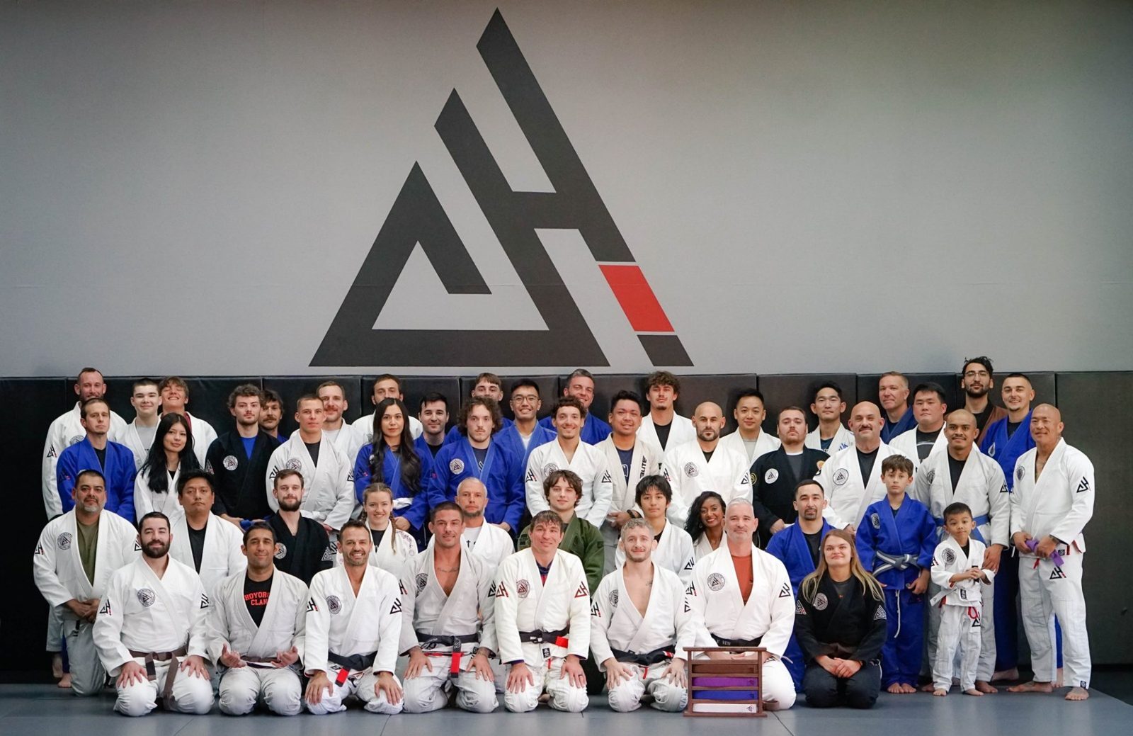 The Holdsworth Jiu Jitsu team in gis in front of the academy logo