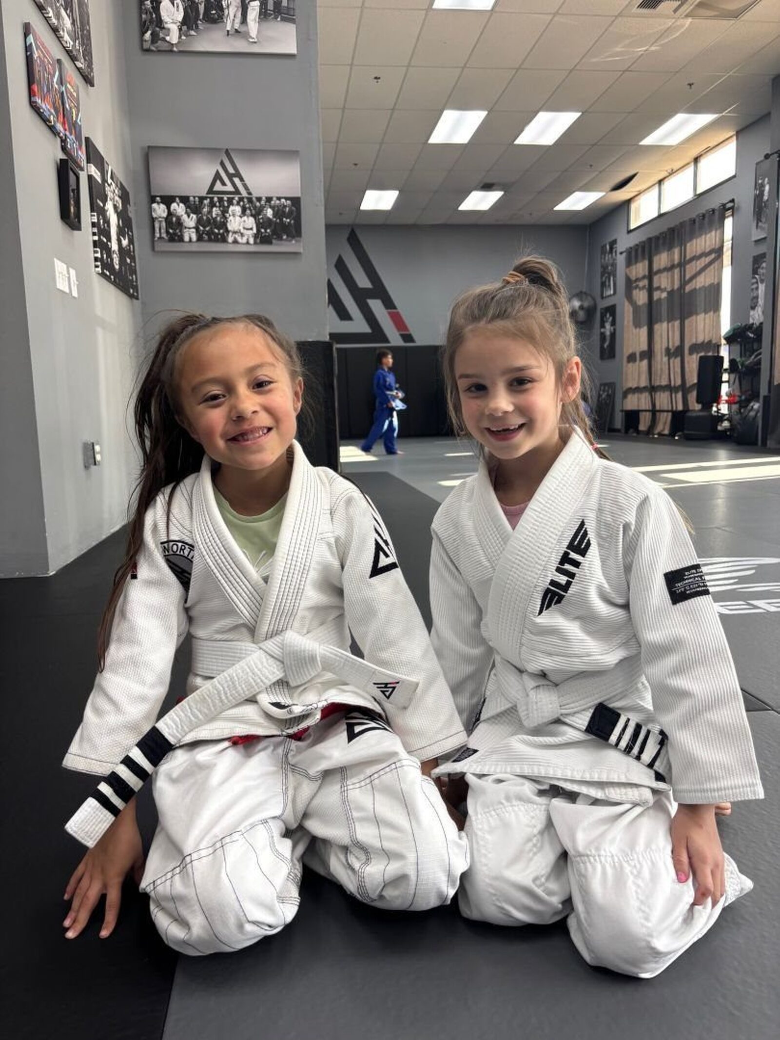 Two smiling girls in white gis at the academy