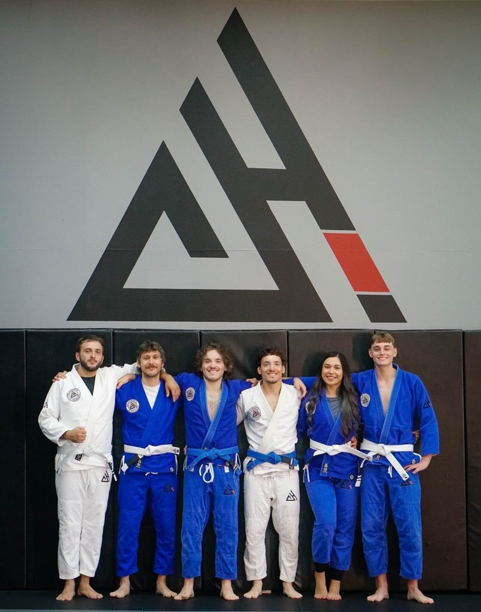 Adult students in blue and white gis in front of the academy logo