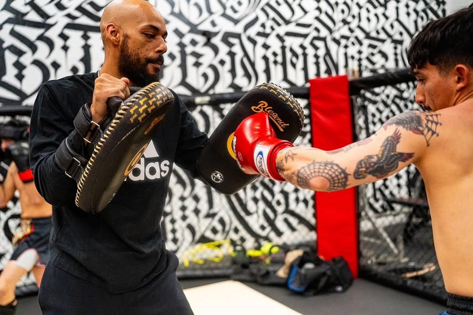 SVG coach holding focus mitts in the cage as a fighter lands a punch