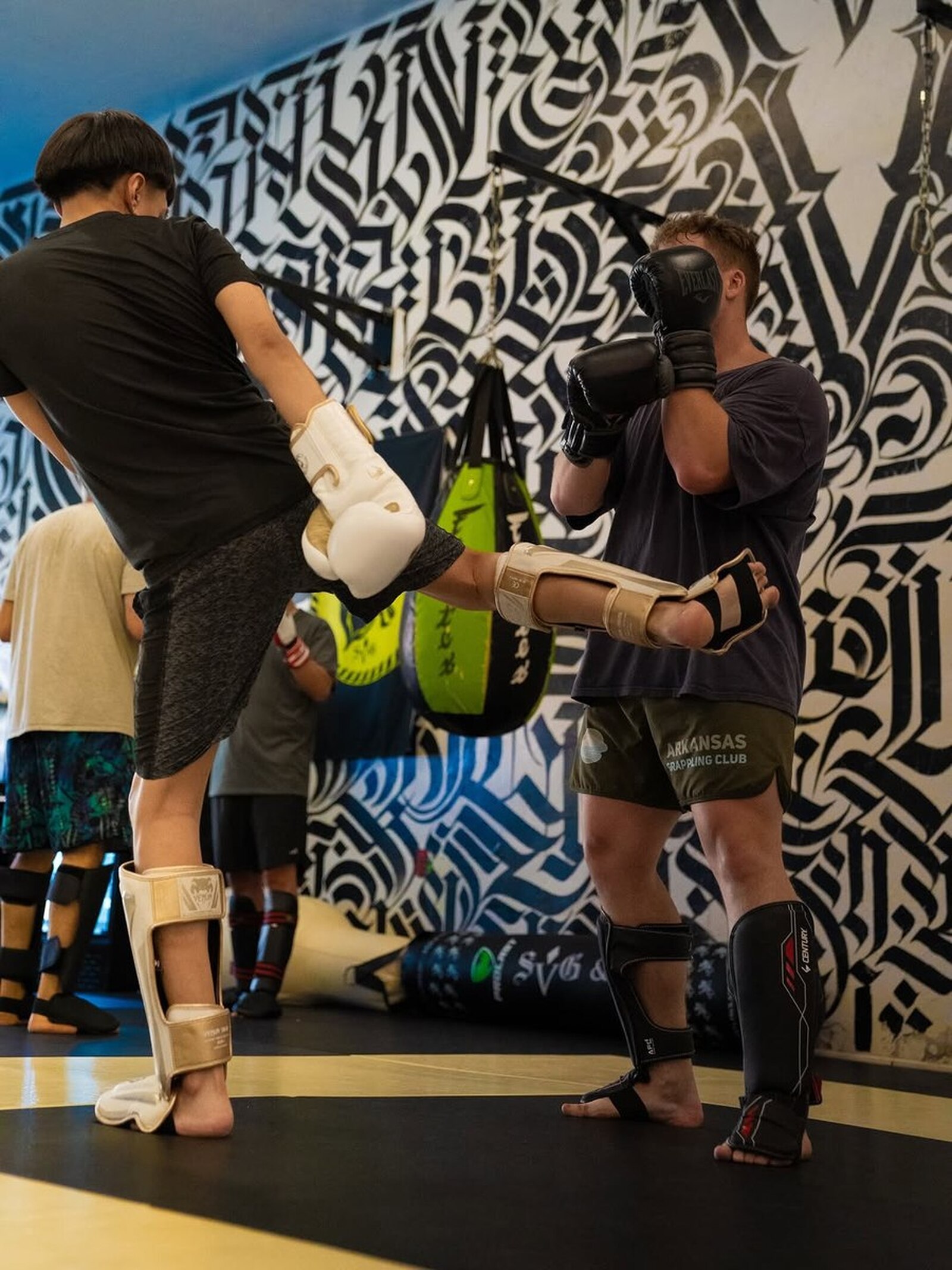 Two SVG members in shin guards sparring in the gym, one catching a kick