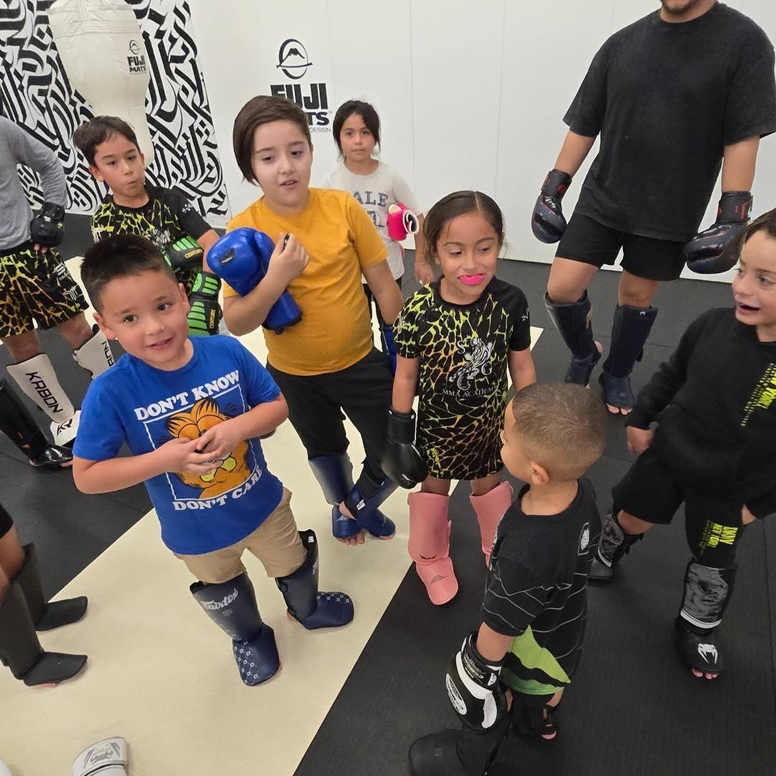 Young SVG kids in gloves and shin guards during kids class with their coach beside them