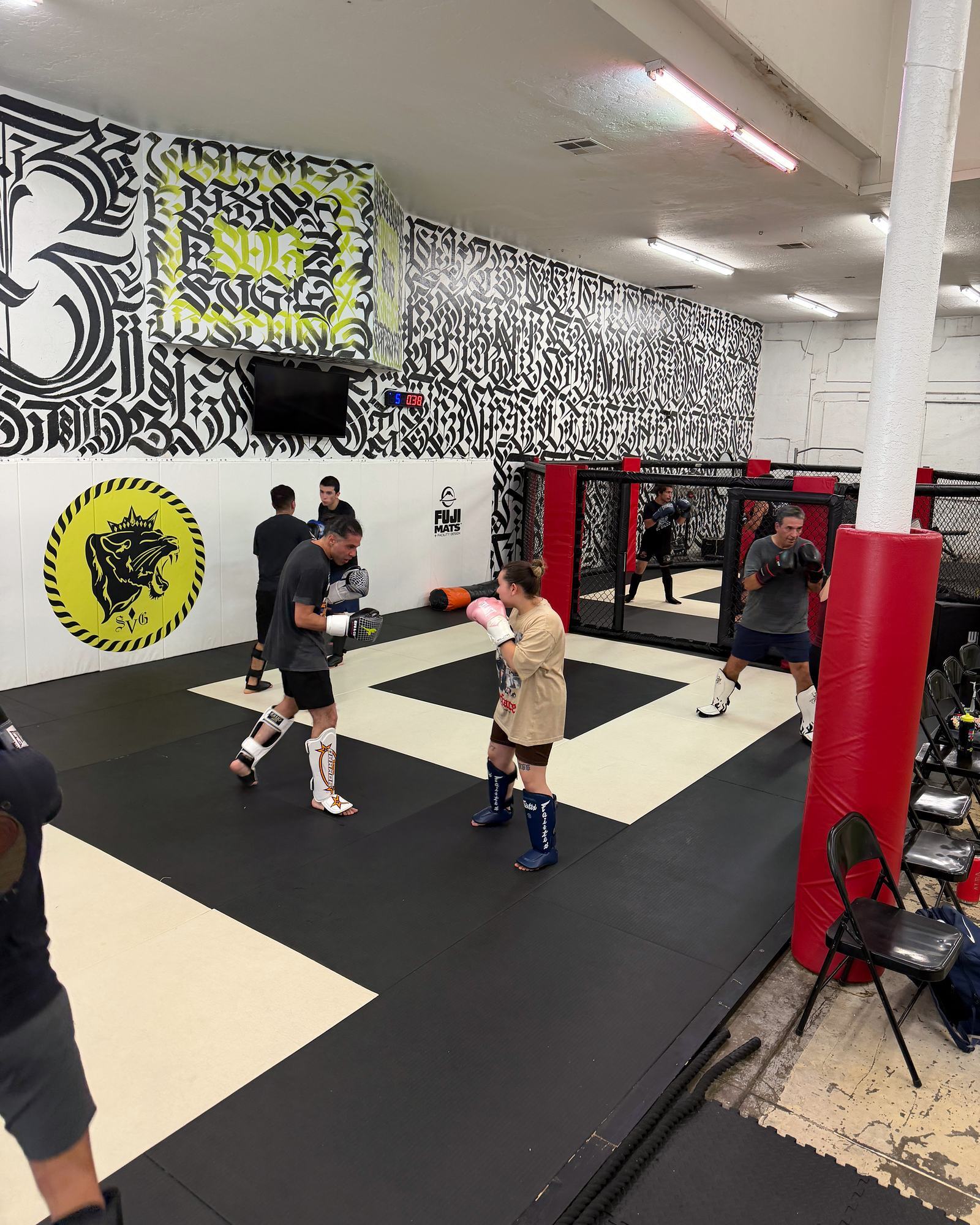 Adult class paired up for striking drills across the SVG mats, with the lime SVG logo, the mural and the cage in the background